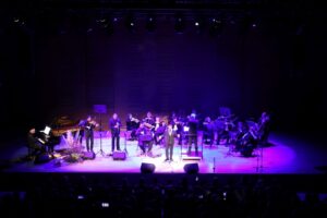 orkiestra na scenie oświtelona kolorowym fioletowo-niebieskim światłem